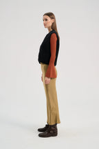 Woman wearing a black wool sweater, rust-colored shirt, beige pants, and brown boots on a white background