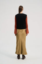 Person wearing a black vest, red long-sleeve shirt, and beige skirt on a white background